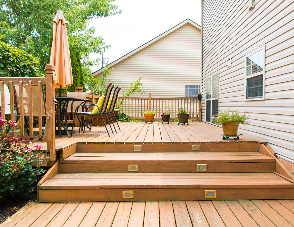 a wooden backyard deck with patio furniture and stairs leading down to the grass