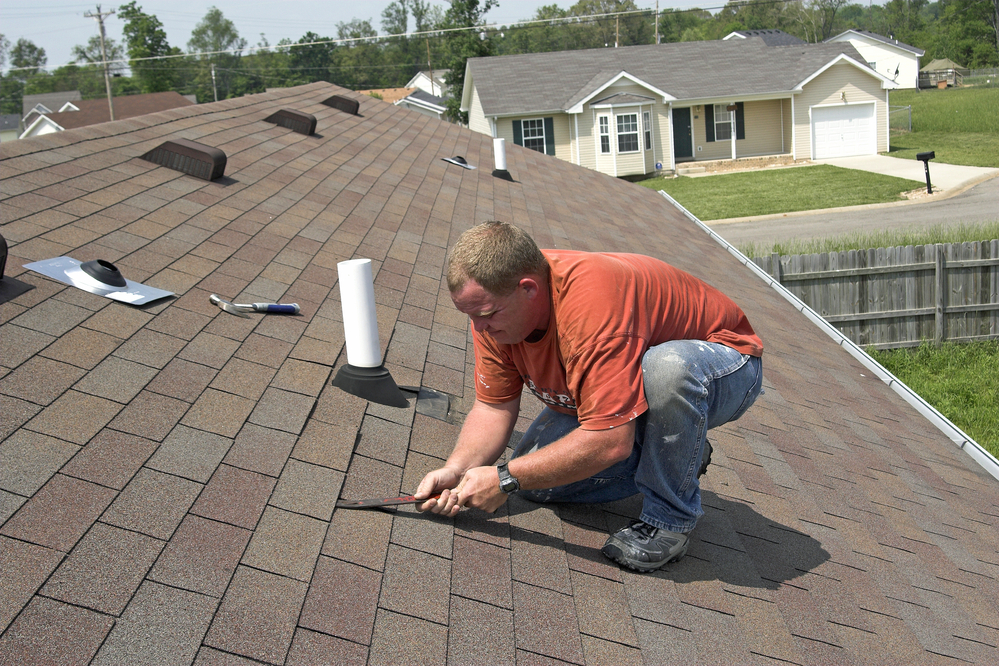 a roofing contractor making repairs on top of a shingle roof