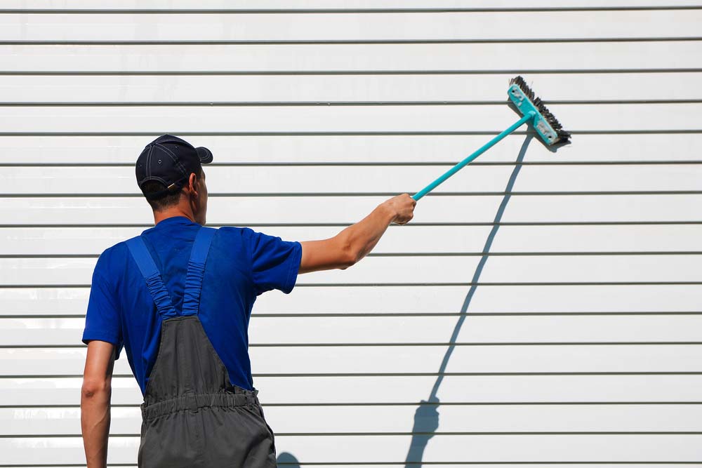 a contractor using a long-handled brush to clean the siding on a house
