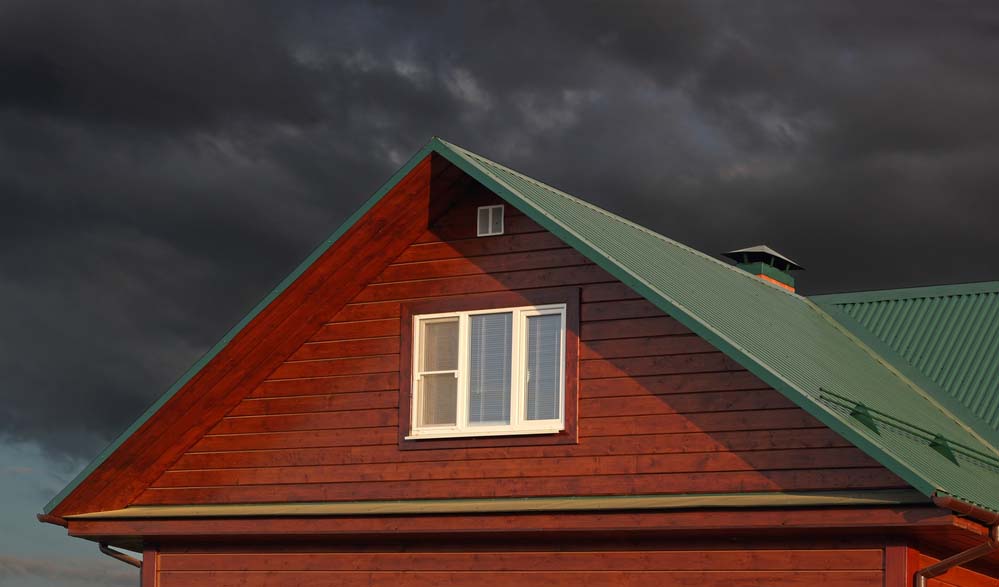a home with a green metal roof under dark storm clouds