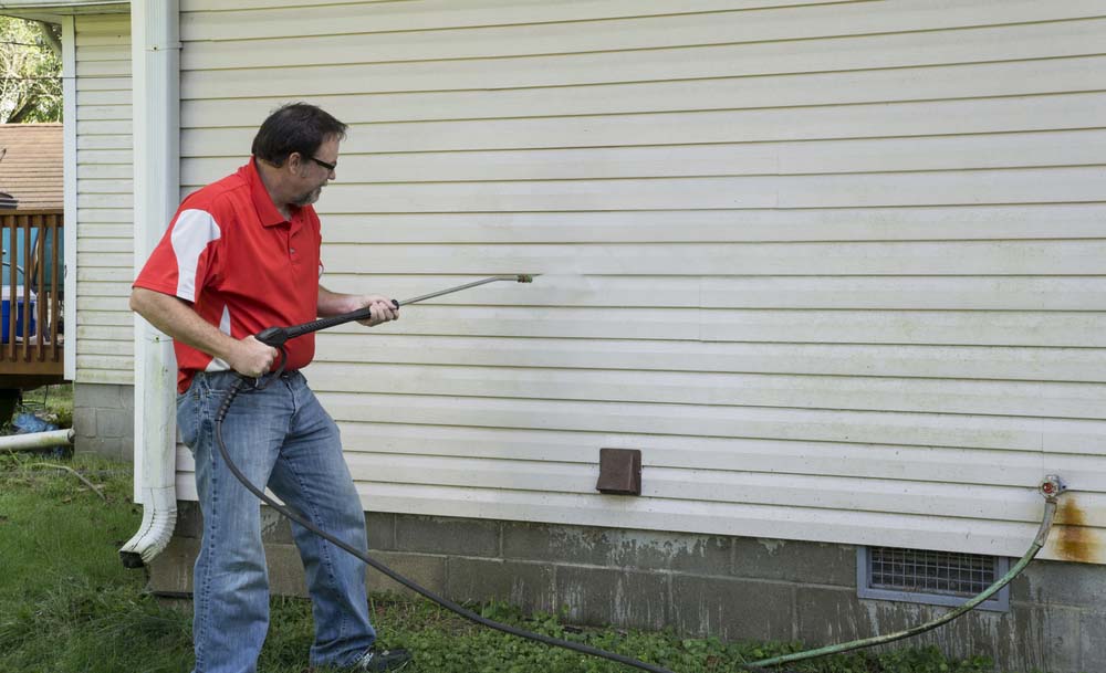 A contractor uses a power washer to clean vinyl siding.