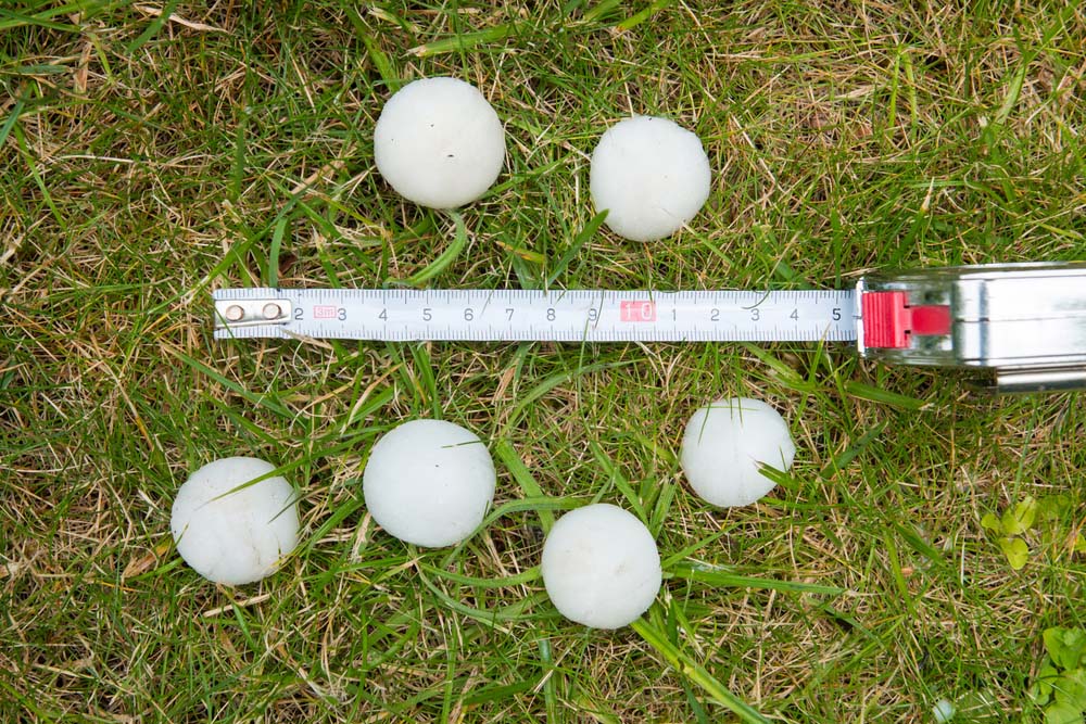 different size hailstones next to a measuring tape on the grass