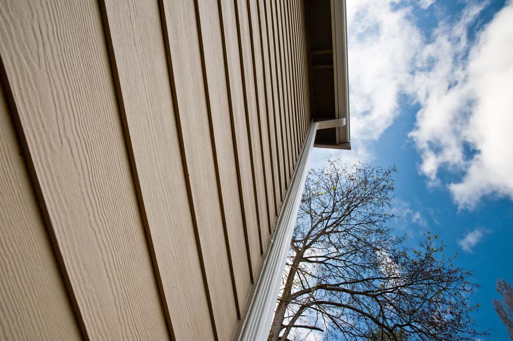 A close-up photo of a house’s siding and downspout taken from below aiming up toward the roofline. 