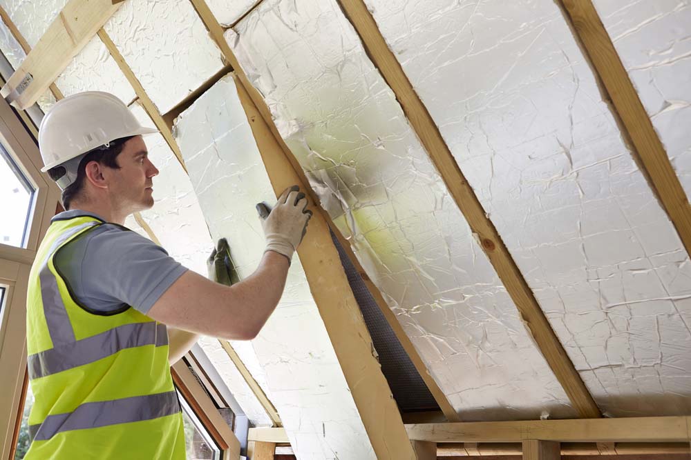A man in a hard hat installs insulation into the roof of a home.