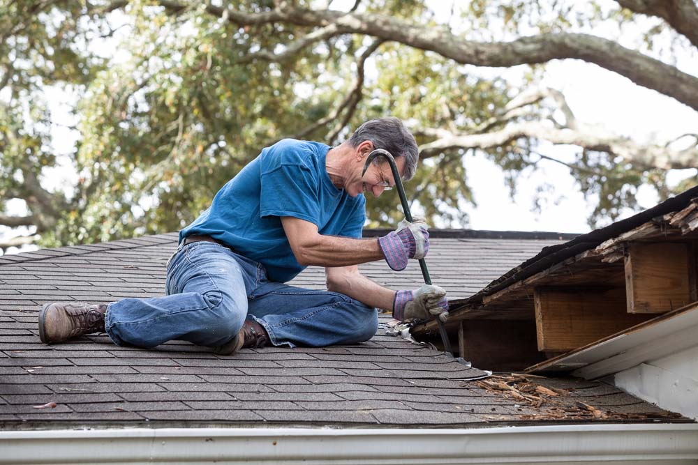 A man repairs a leaking roof with a crowbar.