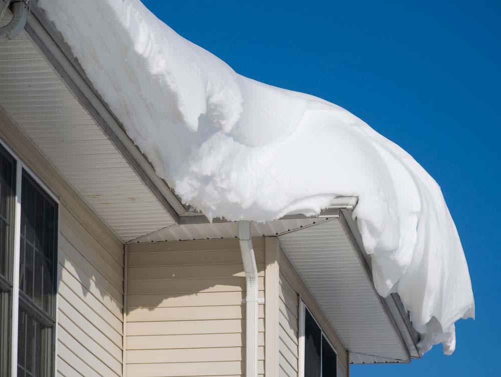 A residential roof with a snowdrift on top, taken from underneath the roof line.
