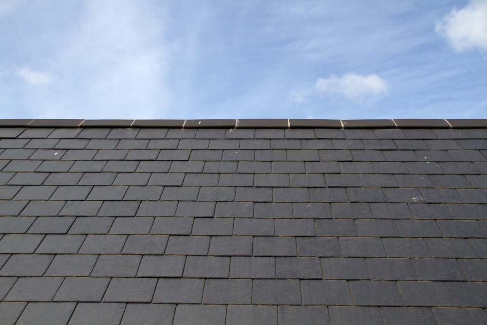 A roof with gray/black slate tiles underneath a blue sky.