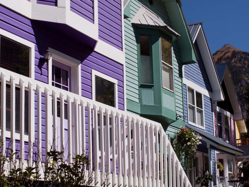 A few row houses with blue, purple, and green vinyl siding sitting next to each other.