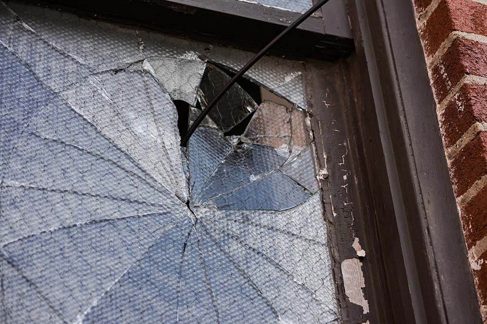 A window with brown frames on a brick house with shattered glass.