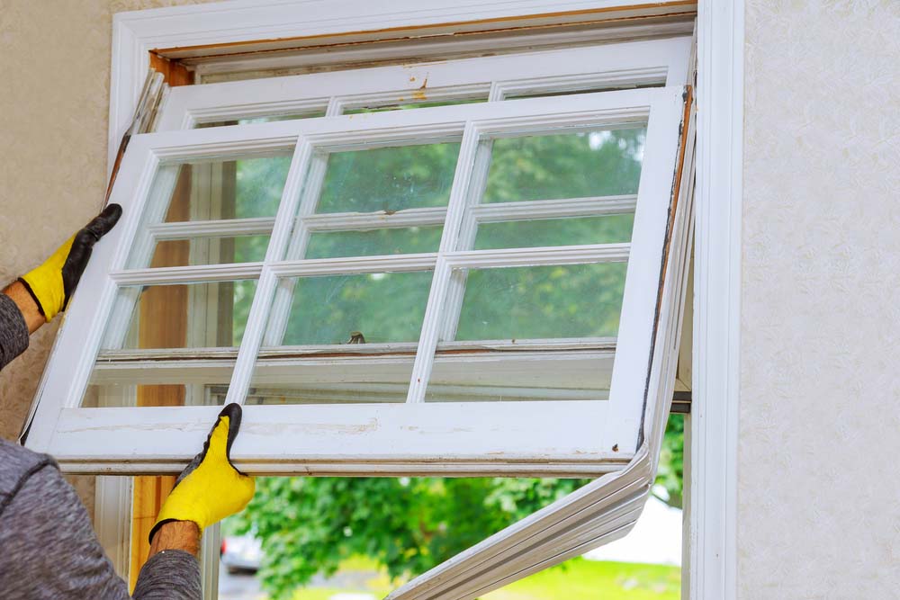 A worker wearing yellow gloves removes an old window from a house’s interior.