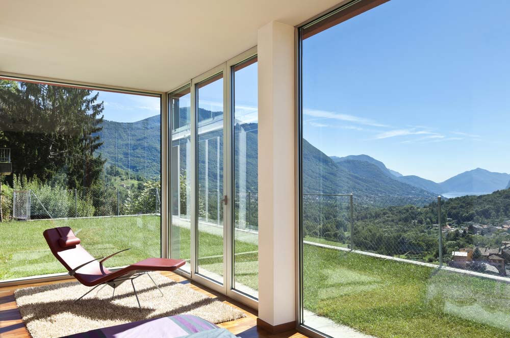 A modern room with floor-to-ceiling windows overlooking green land and mountains.